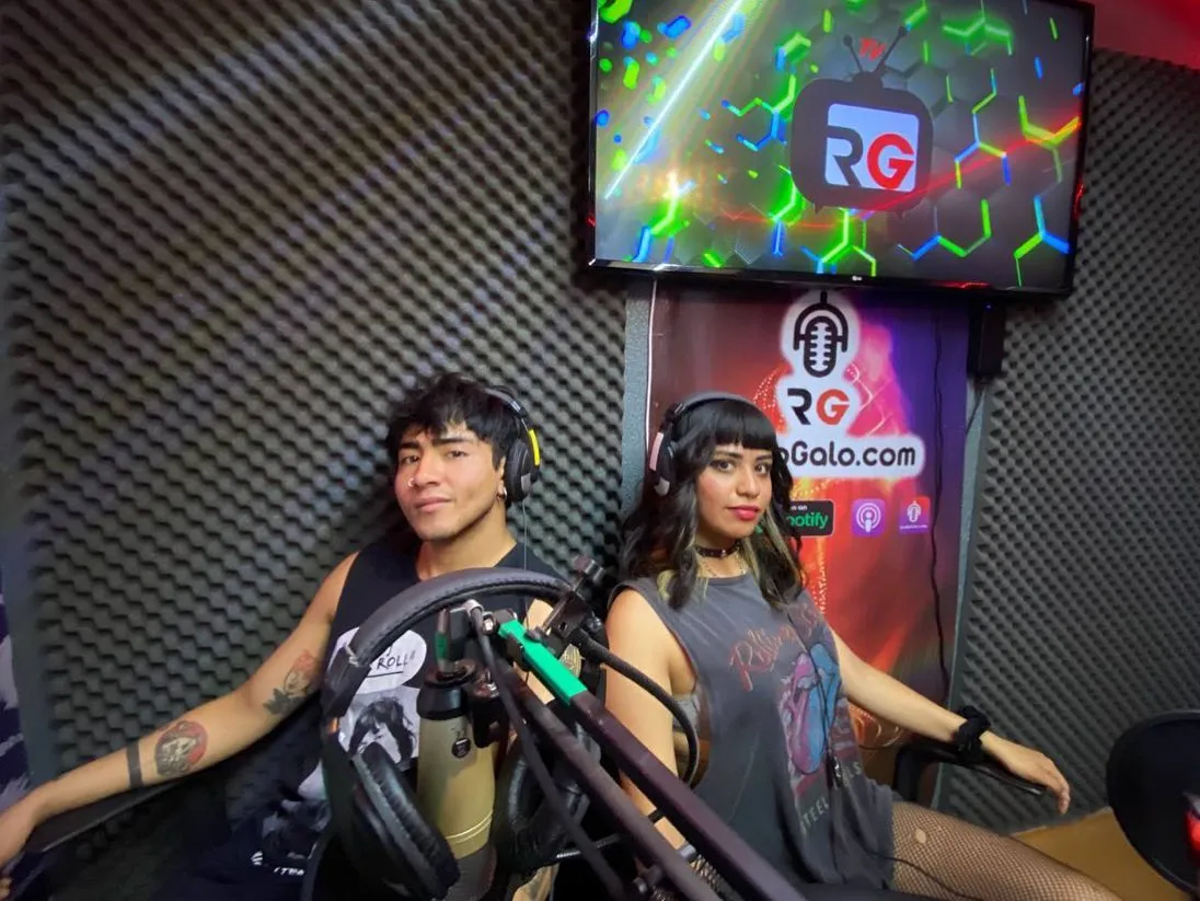 Dos invitados en la cabina, frente a micrófonos de condensador y la pantalla con el logo de Radio Galo