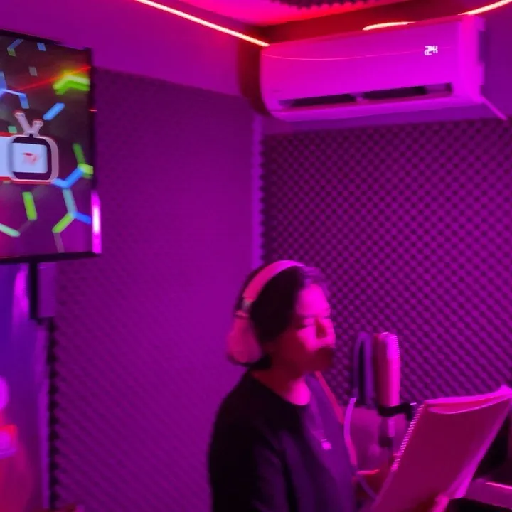 Cantante grabando con audífonos frente a un micrófono de condensador, en la cabina morada