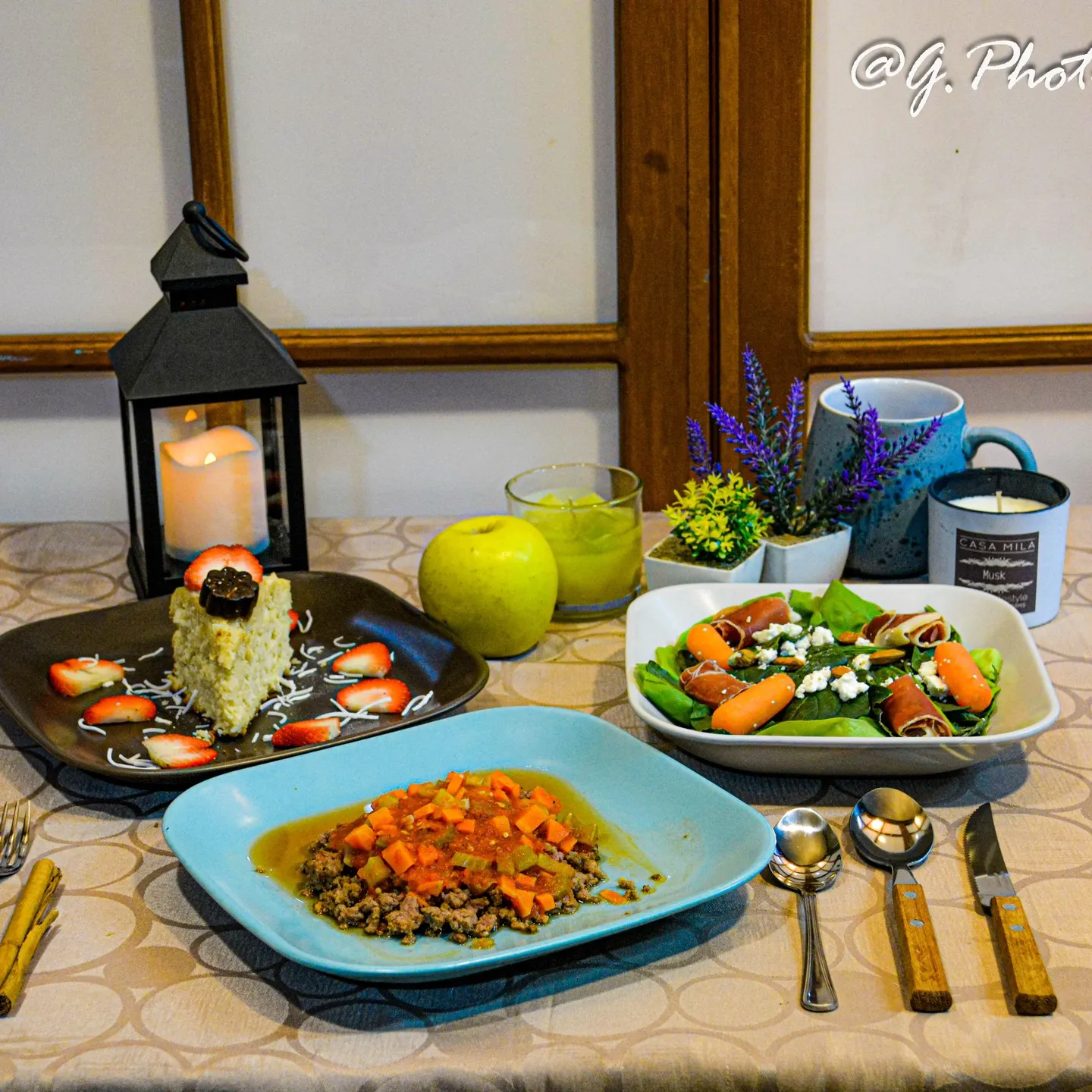 Mesa servida con ensalada, guisado, postre y velas