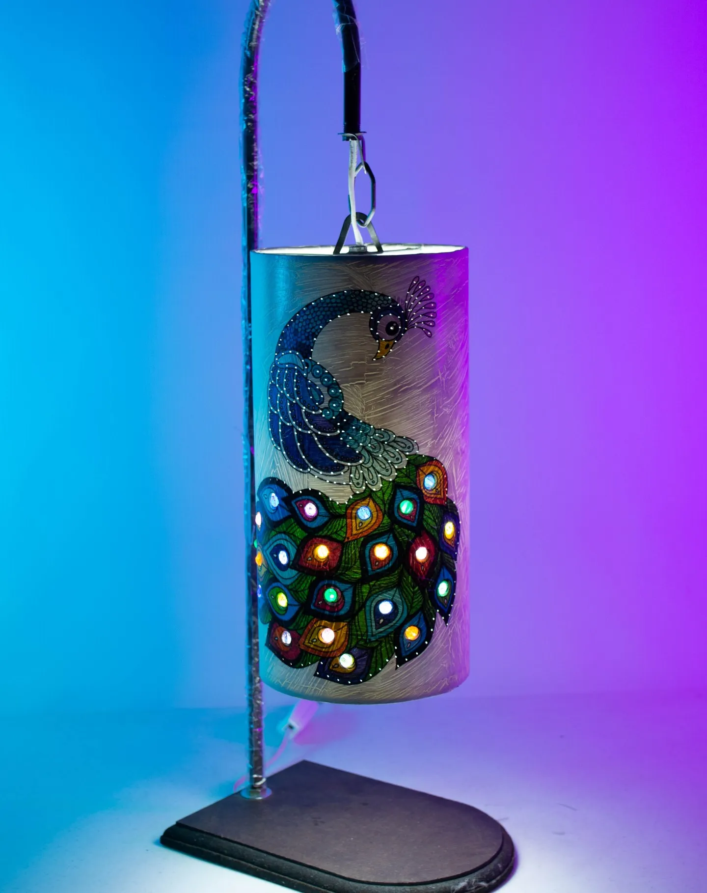 Lámpara artesanal con un pavorreal sobre fondo azul y morado
